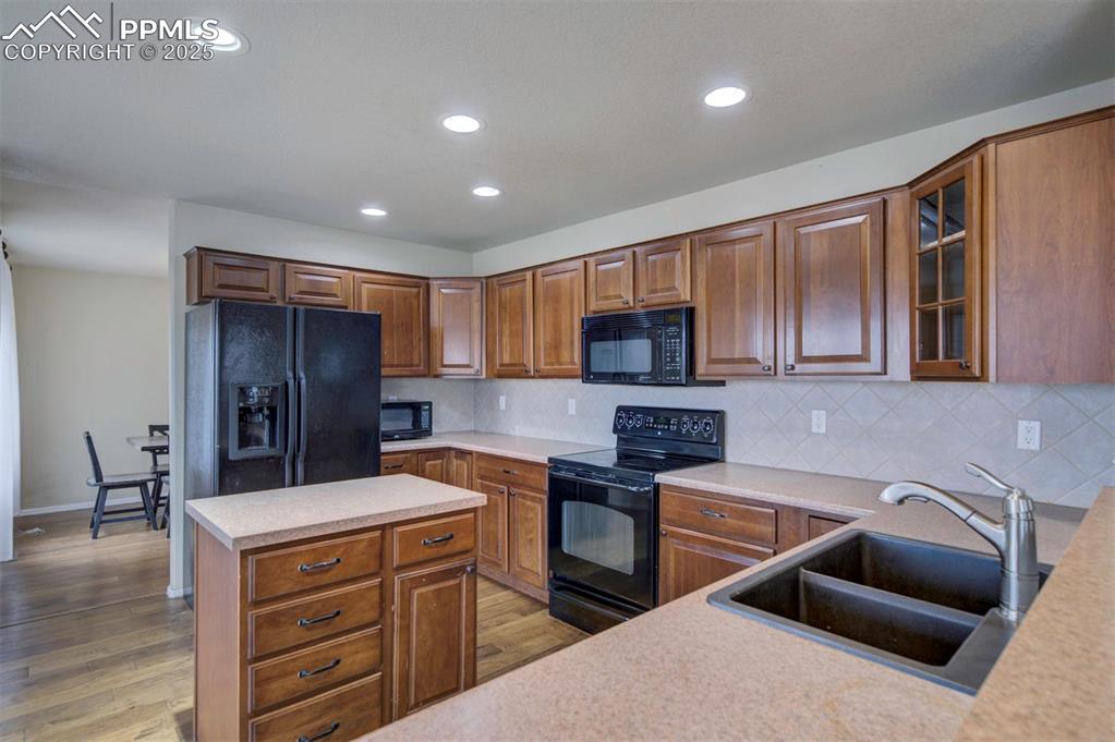 Image 16 of 43: Kitchen featuring black appliances, a sink, light countertops, backsplash,