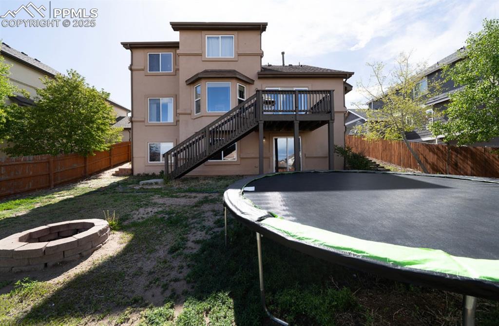 Image 42 of 43: Back of property with a trampoline, an outdoor fire pit, stairs, a fenced b