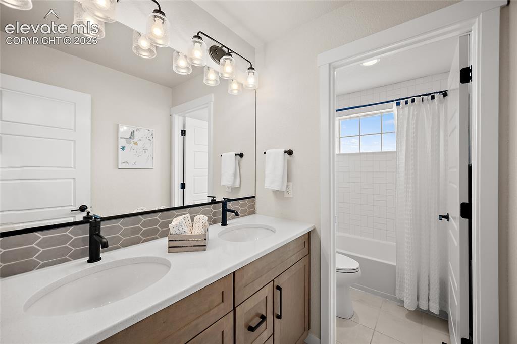 Image 31 of 47: Double vanity with white countertops, wood-finish cabinetry, and matte blac