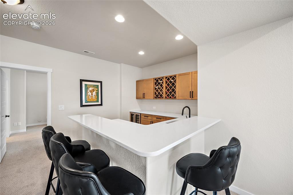 Image 38 of 47: Built-in wet bar featuring a white countertop, wood cabinetry, integrated w
