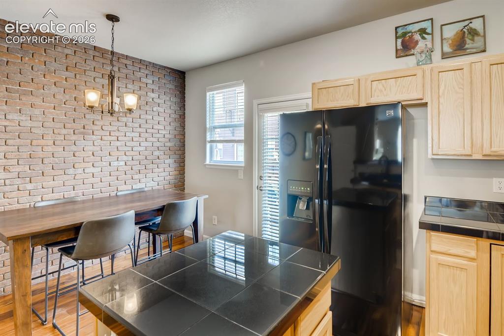 Image 11 of 23: Kitchen featuring a prominent brick accent wall, light wood cabinetry, blac