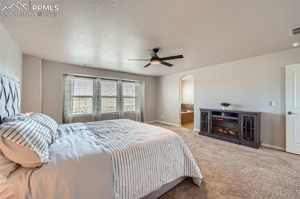 Image 15 of 29: Bedroom with arched walkways, carpet, baseboards, a fireplace, and a ceilin
