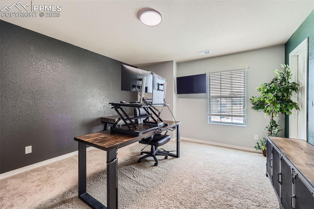 Image 22 of 29: Office area featuring light colored carpet, baseboards, and a textured wall