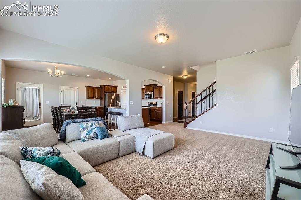 Image 6 of 29: Living room with arched walkways, a chandelier, stairs, light colored carpe