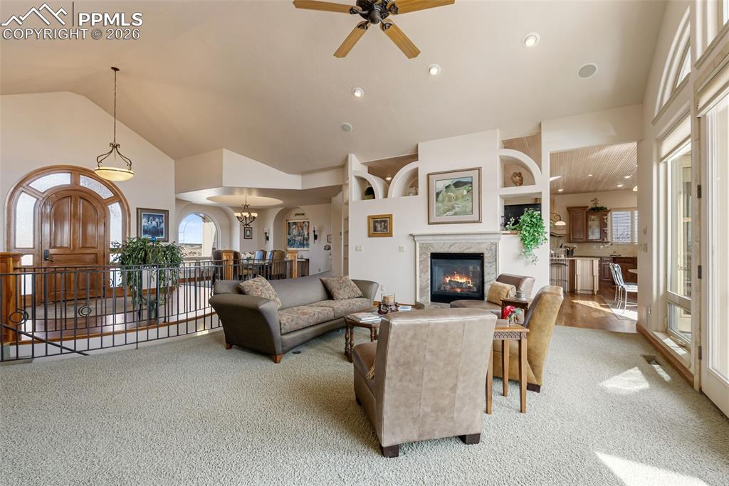 Image 8 of 50: Carpeted living area with ceiling fan, lofted ceiling, a high end fireplace