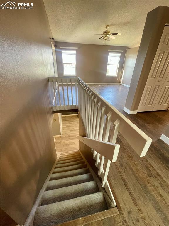 Image 18 of 29: Stairs featuring wood finished floors, a textured ceiling, and a ceiling fa