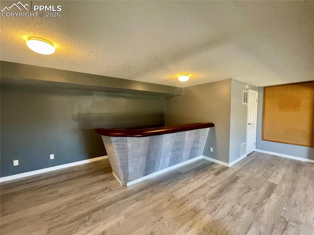 Image 21 of 29: Indoor dry bar with a textured ceiling, light wood-type flooring, and dark 