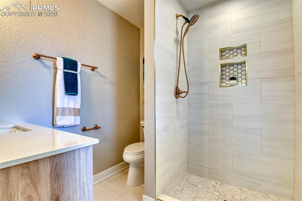Image 22 of 35: Full bathroom with a textured wall, vanity, and a tile shower