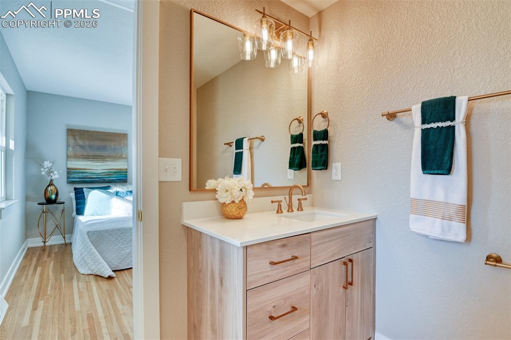 Image 23 of 35: Ensuite bathroom with vanity, light wood-style floors, and a textured wall