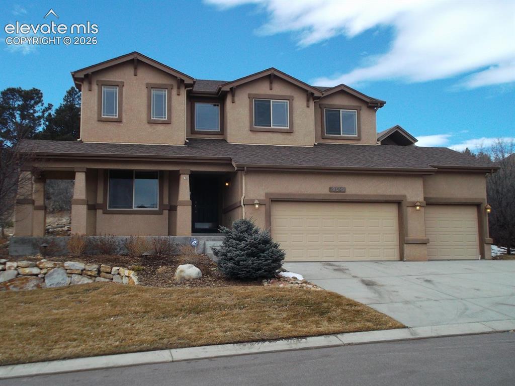 Caption: Two-story stucco home featuring a tan exterior with brown tile roof accents, dual two-car garage doo