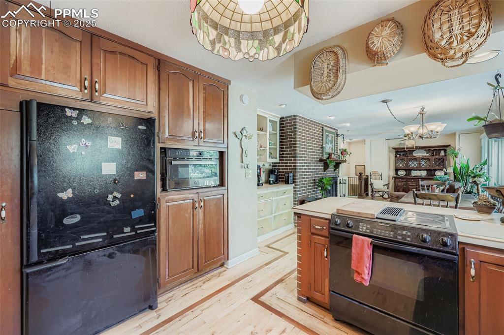 Image 7 of 23: Kitchen with black appliances, brown cabinets, light countertops, a chandel