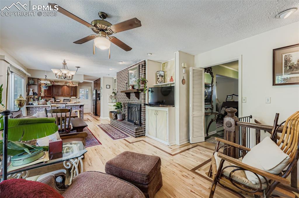 Image 8 of 23: Living area with light wood-style flooring, a brick fireplace, a textured c