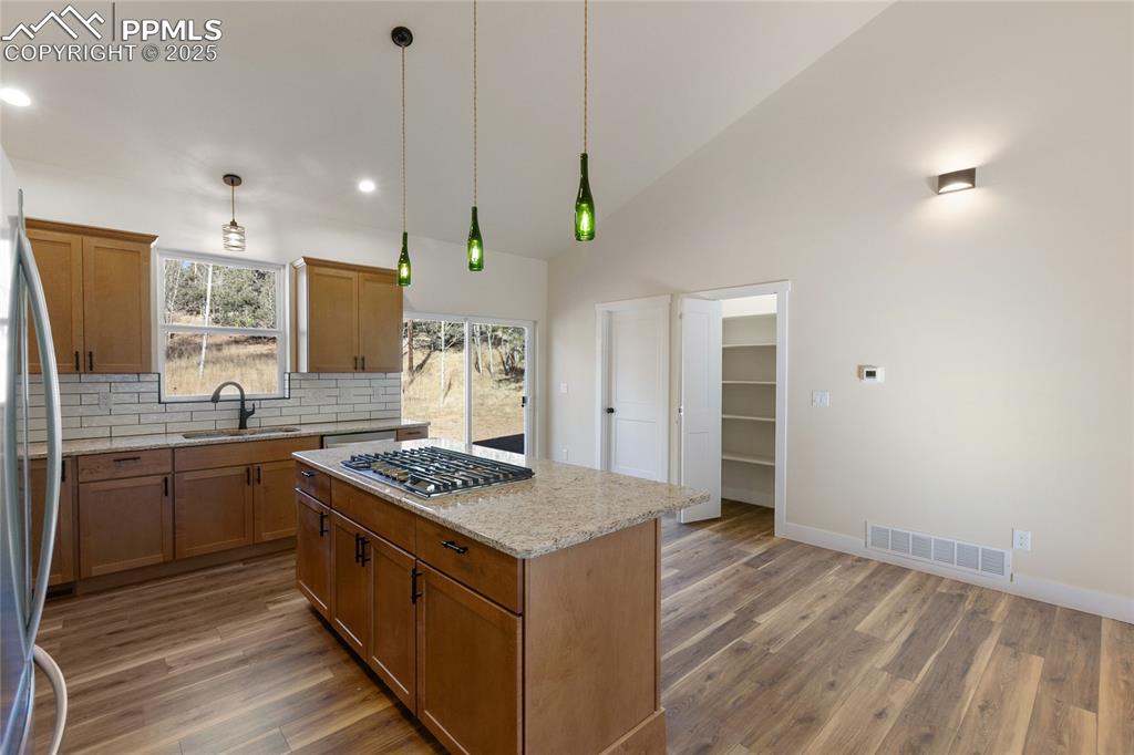 Image 14 of 38: Kitchen featuring brown cabinets, light stone counters, decorative backspla