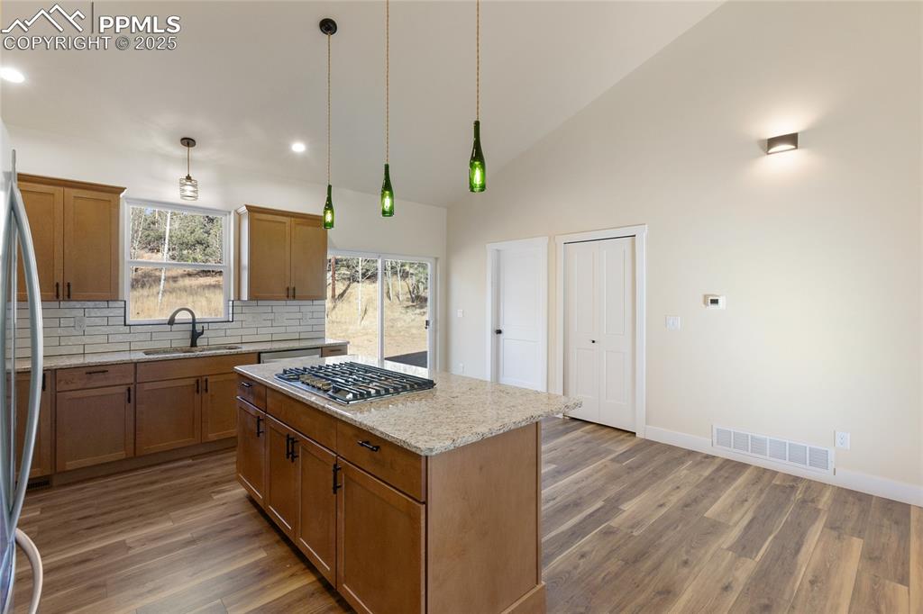 Image 17 of 38: Kitchen with brown cabinetry, light stone countertops, decorative backsplas