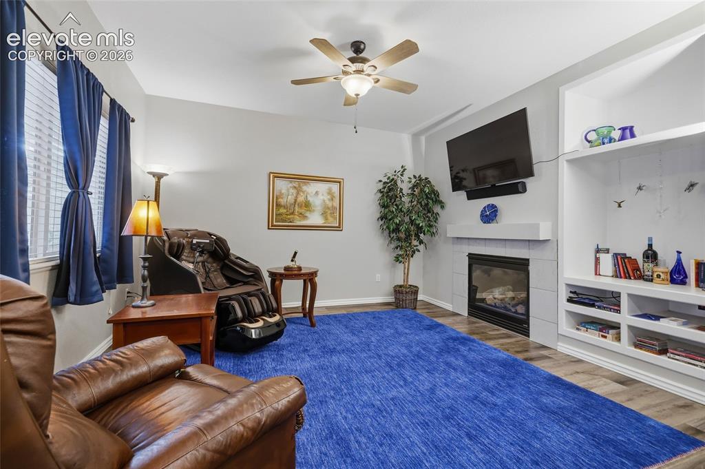 Image 12 of 41: Living area featuring wood-finish flooring, a ceiling fan, and a fireplace