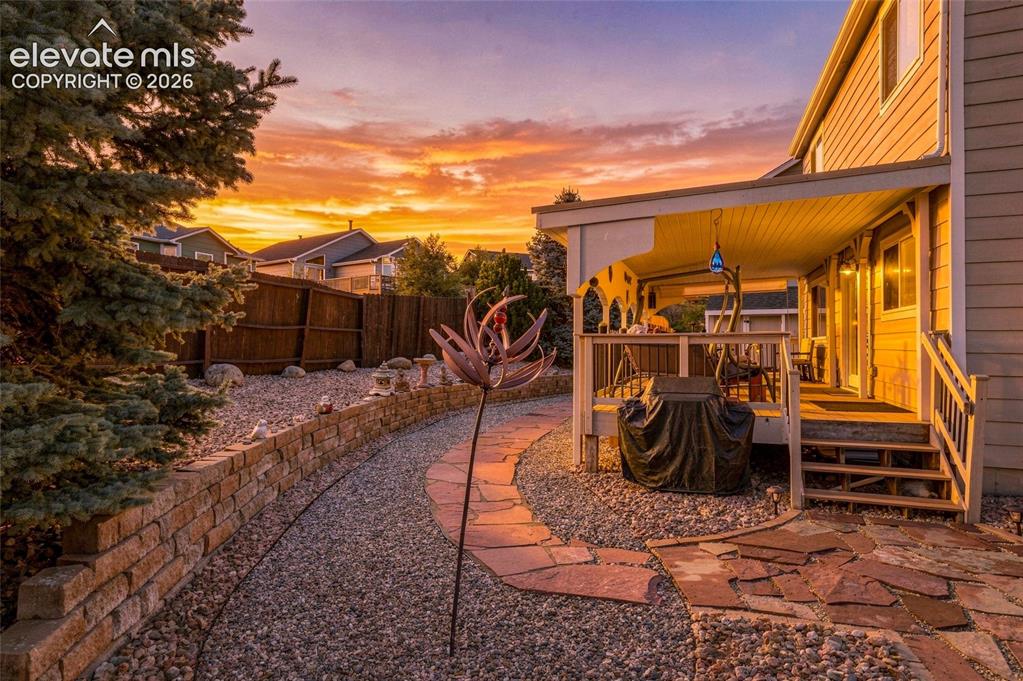 Image 25 of 41: Covered patio with a wood-finish deck and railings, stone paver pathway, gr