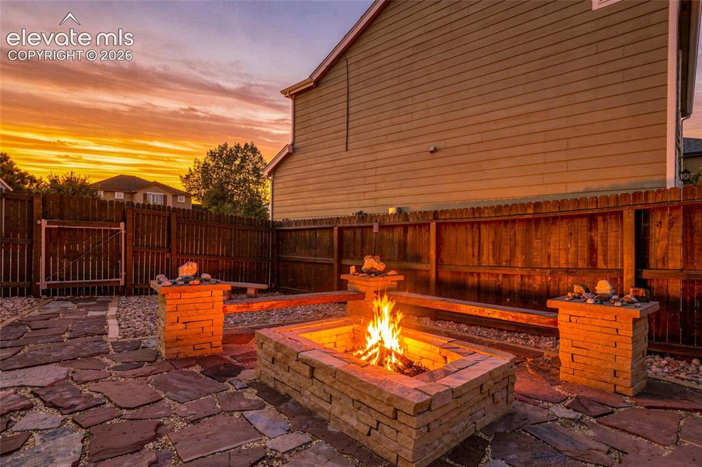 Image 27 of 41: Flagstone patio with a built-in stone fire pit, wood fencing, and stone pil