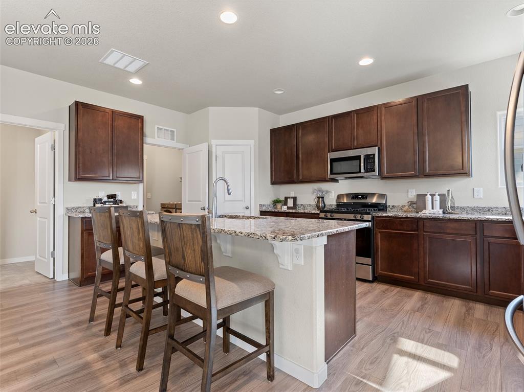 Image 14 of 46: Kitchen featuring wood-finish flooring, dark wood cabinetry, granite counte
