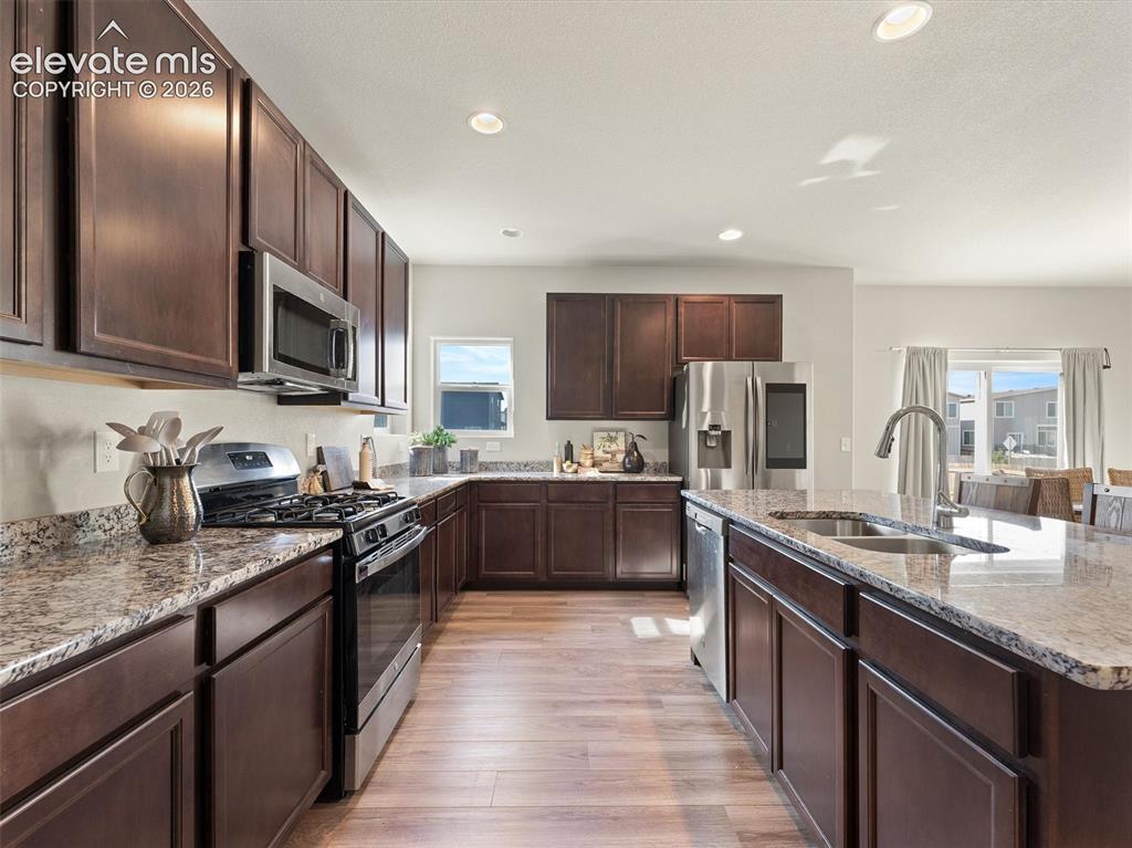 Image 17 of 46: Modern kitchen featuring rich cabinetry, stone countertops, stainless steel