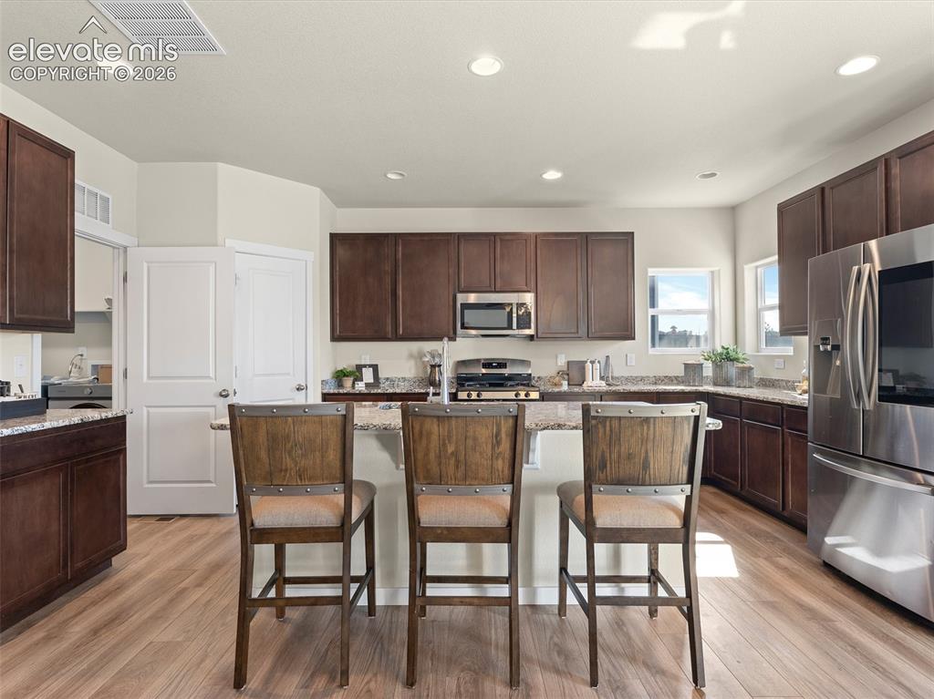 Image 18 of 46: Kitchen featuring wood-finish flooring, dark wood cabinetry, and granite co