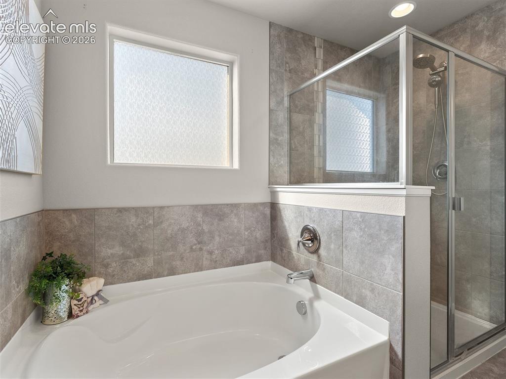Image 31 of 46: Corner soaking tub featuring chrome fixtures, a privacy window, and tiled s