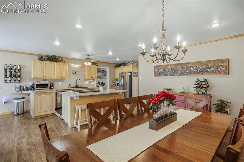 Image 17 of 50: Dining area with crown molding, ceiling fan, hanging lights, and light wood