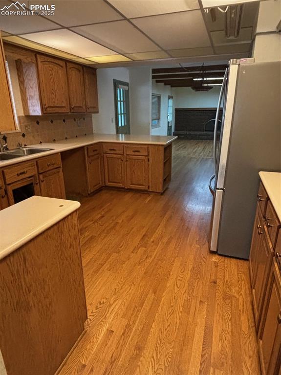 Image 4 of 17: Kitchen featuring brown cabinets, refrigerator, a peninsula, and light coun