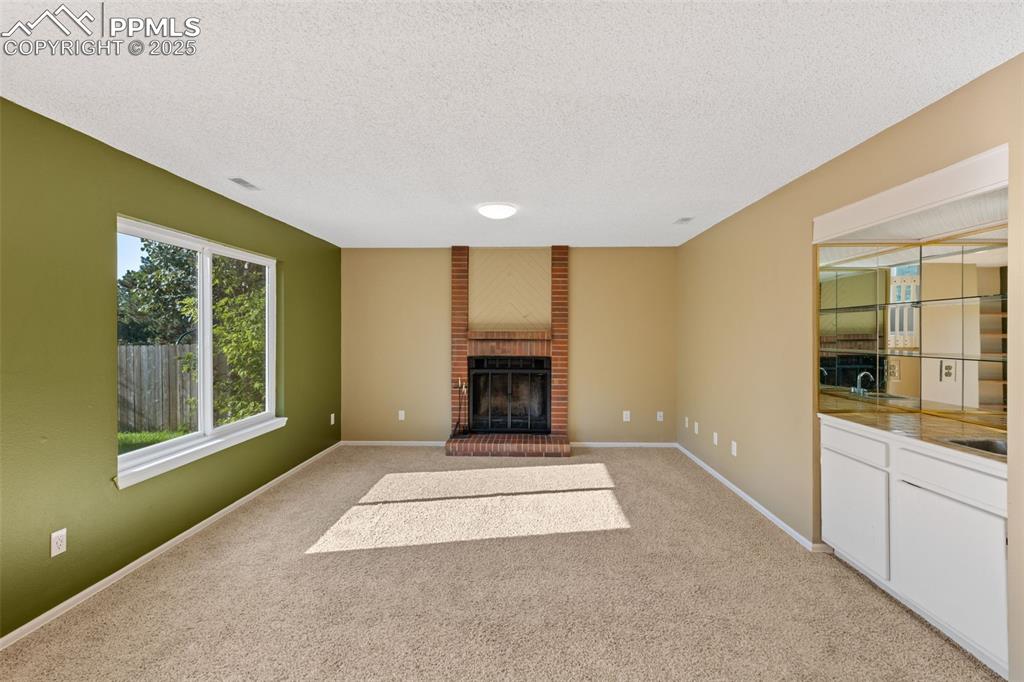 Image 11 of 33: Unfurnished living room featuring a brick fireplace, light carpet, and a te