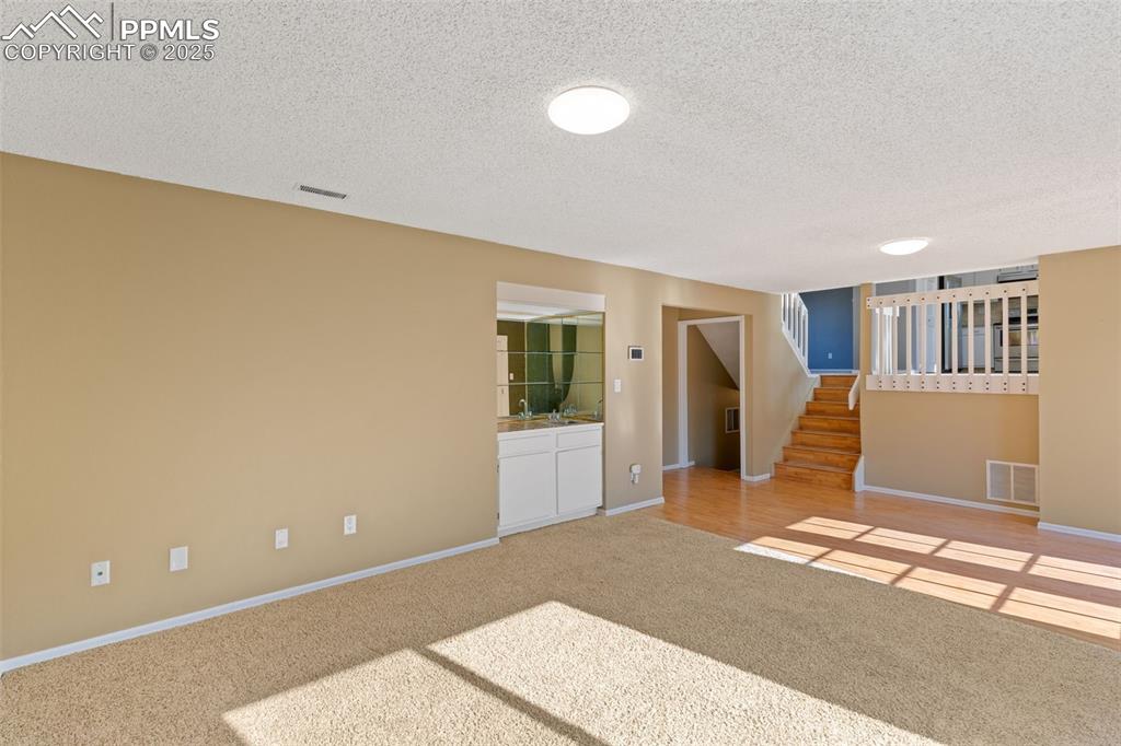 Image 12 of 33: Empty room with light colored carpet, stairway, and a textured ceiling
