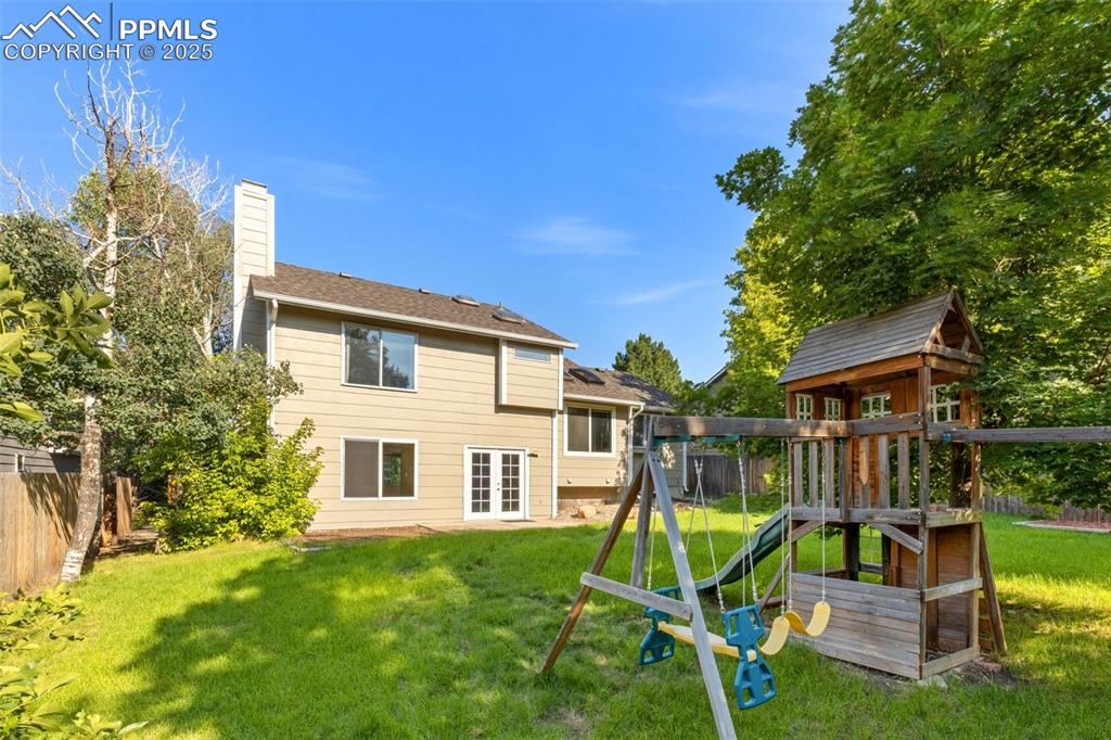 Image 23 of 33: Back of house featuring a playground, a chimney, and a fenced backyard