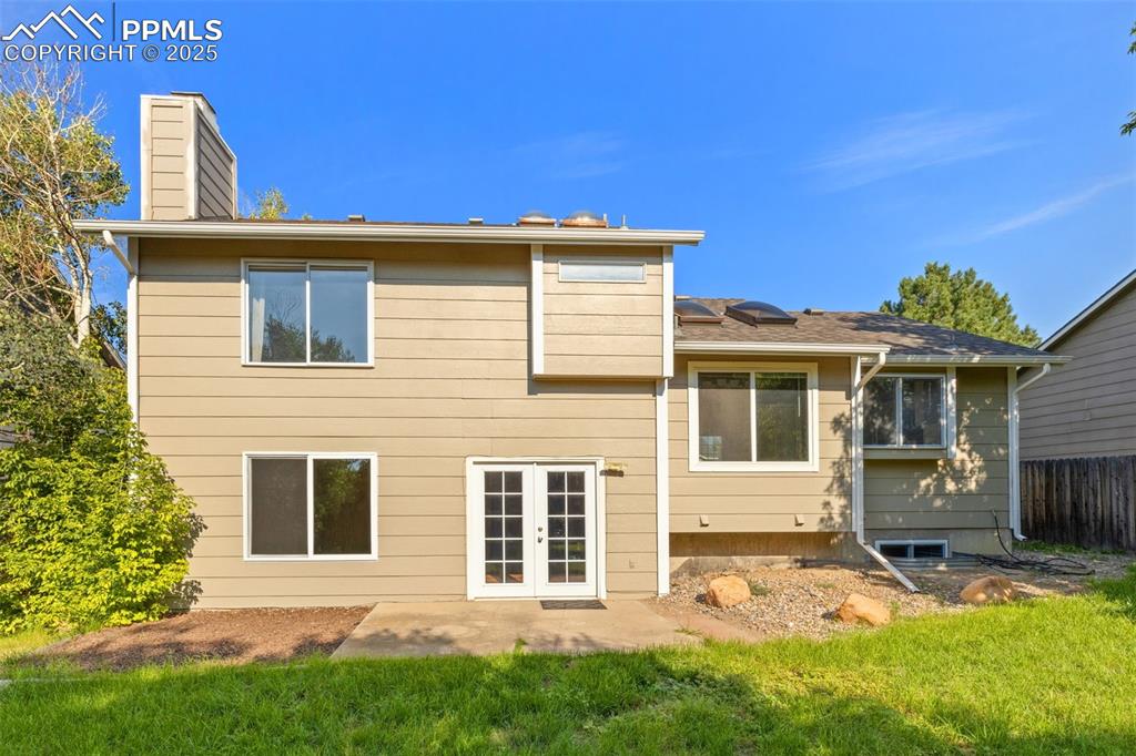 Image 24 of 33: Back of house featuring a chimney, french doors, solar panels, and a patio