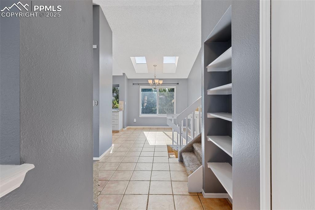 Image 5 of 33: Hall featuring a textured wall, a skylight, a chandelier, light tile patter