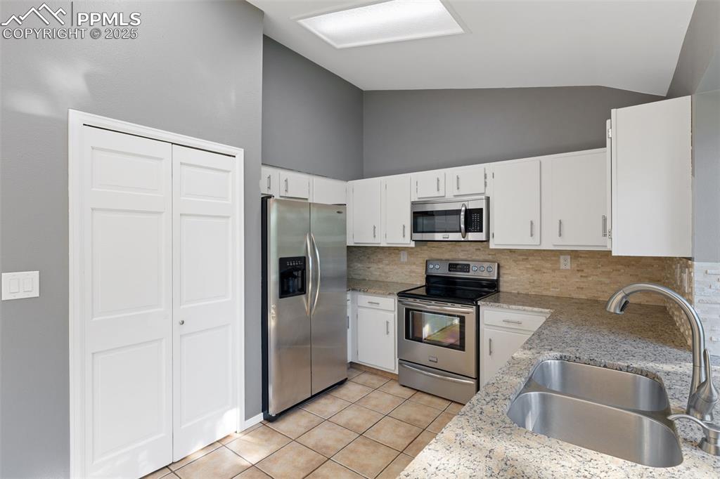 Image 8 of 33: Kitchen with stainless steel appliances, lofted ceiling, decorative backspl