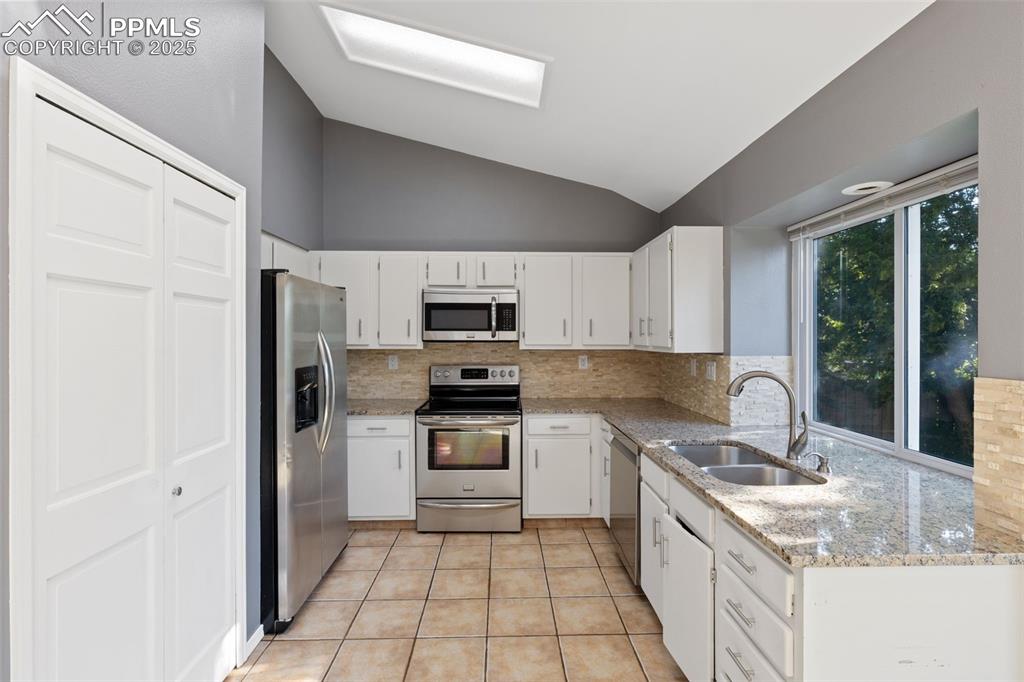 Image 9 of 33: Kitchen with stainless steel appliances, backsplash, lofted ceiling, light