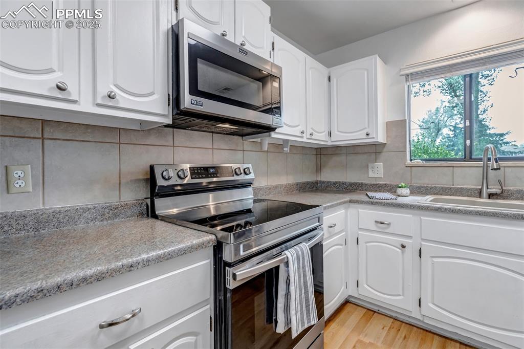 Image 10 of 37: Kitchen featuring stainless steel appliances, white cabinets, light wood-st