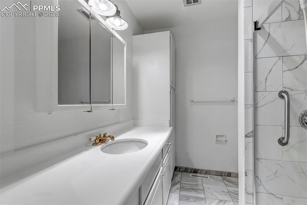 Image 16 of 37: Bathroom featuring vanity, a marble finish shower, and marble look tiles