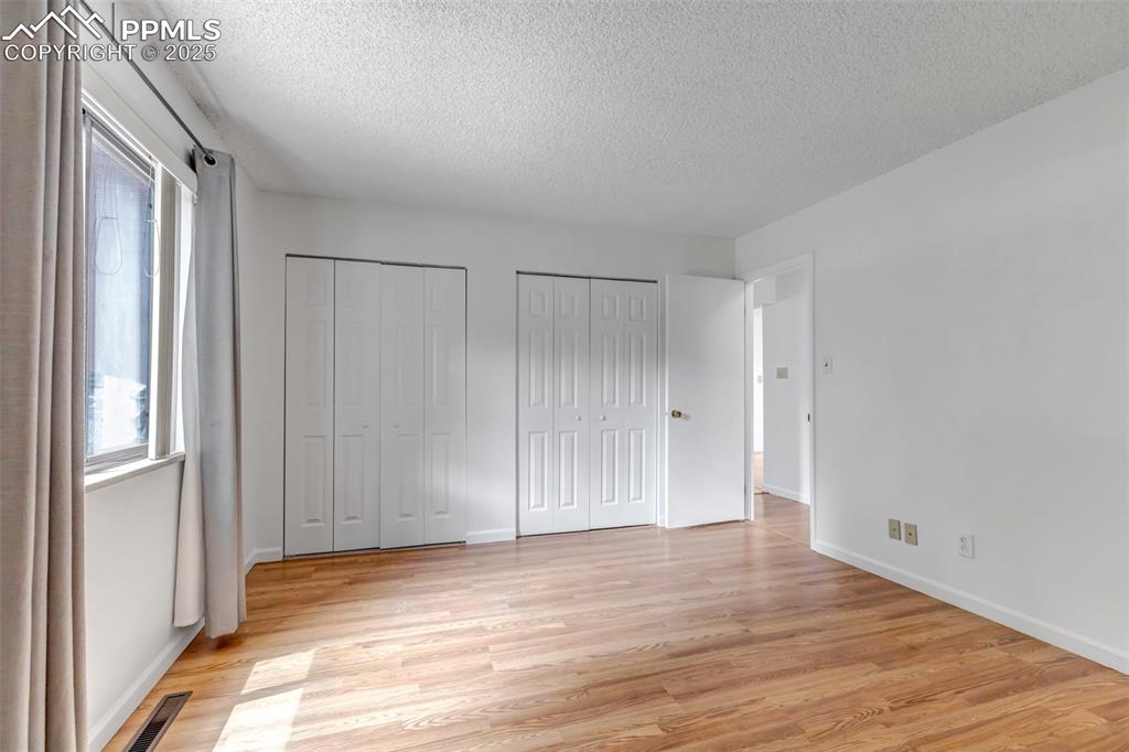 Image 20 of 37: Unfurnished bedroom featuring two closets, a textured ceiling, and light wo