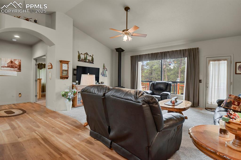 Image 11 of 43: Living area featuring arched walkways, ceiling fan, a wood stove, vaulted c