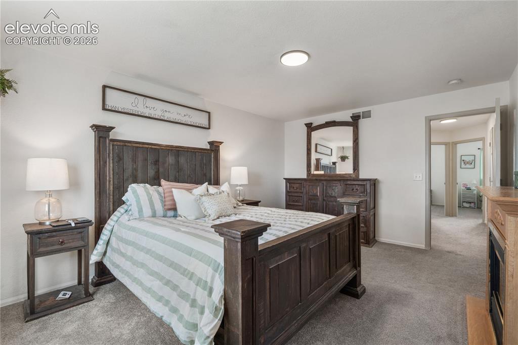 Image 23 of 41: Spacious sleeping area featuring light gray carpet, a built-in fireplace wi