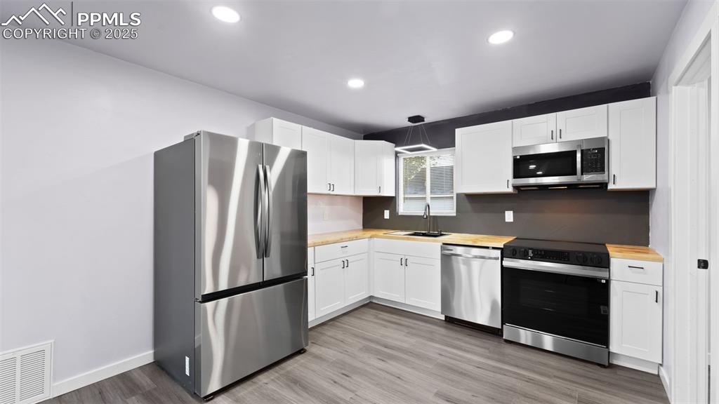 Image 10 of 28: Kitchen with stainless steel appliances, white cabinets, light wood-style f