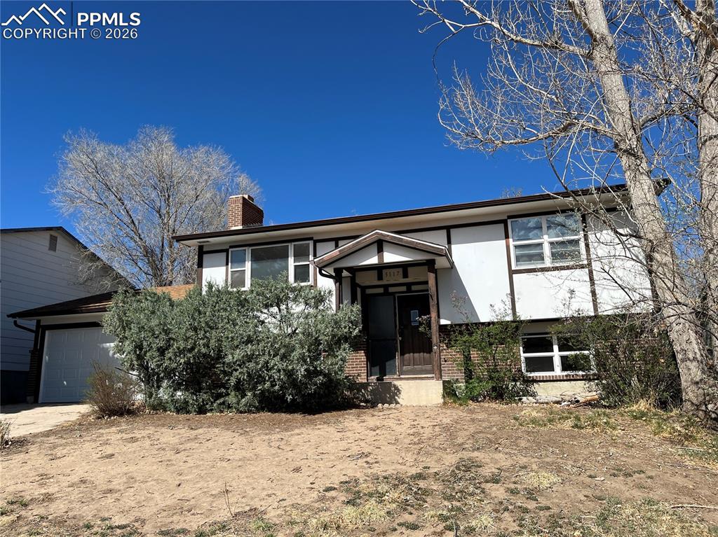 Image 1 of 13: Raised ranch featuring brick siding, a chimney, a garage, and stucco siding