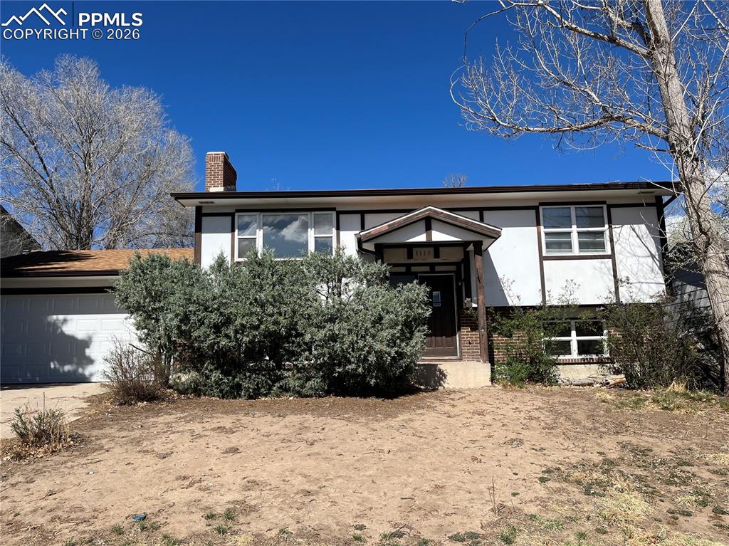 Image 12 of 13: Split foyer home featuring a chimney, brick siding, an attached garage, and