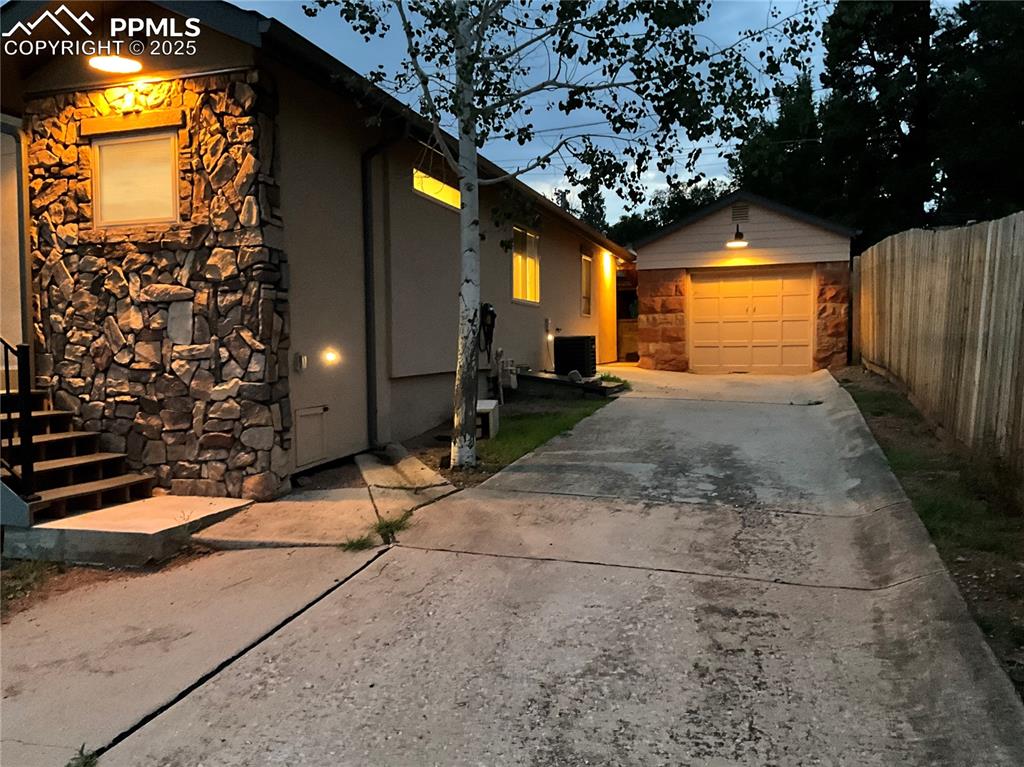 Image 49 of 50: View of side of home featuring stone siding, concrete driveway, an outbuild