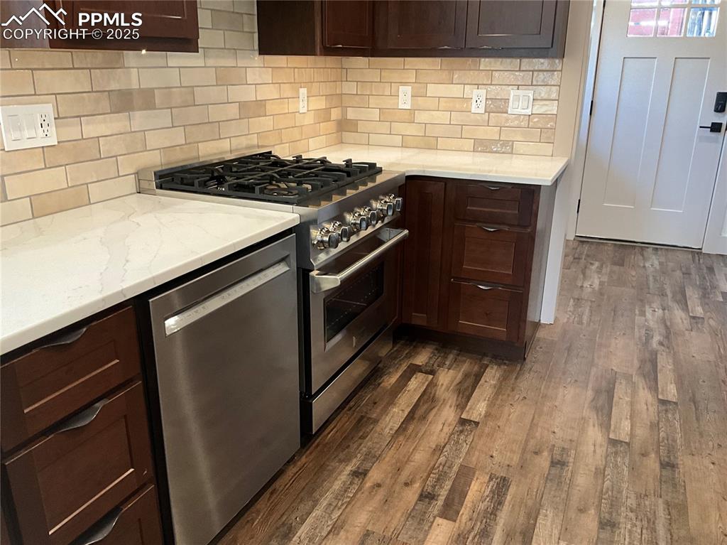Image 8 of 50: Kitchen with stainless steel appliances, dark wood-style flooring, and tas