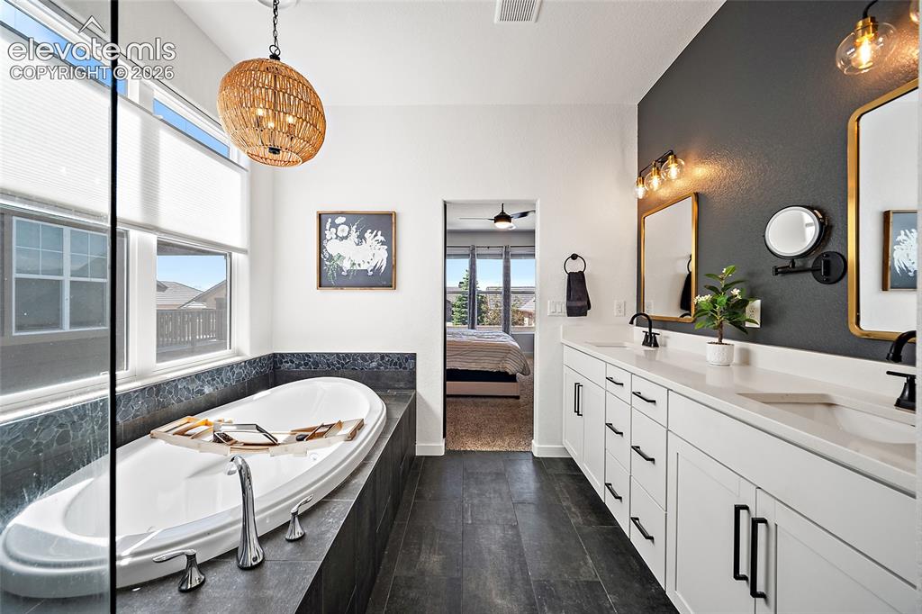 Image 19 of 46: Soaking tub with a tiled surround, dual windows with roller shades, a woven