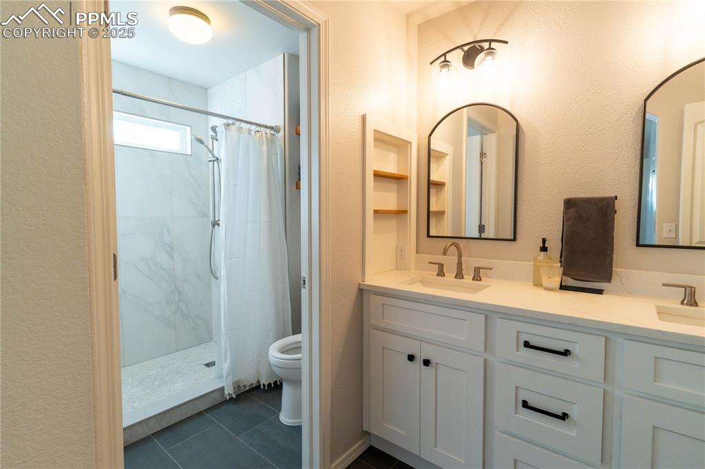Image 12 of 26: Full bathroom featuring a stall shower, double vanity, dark tile patterned
