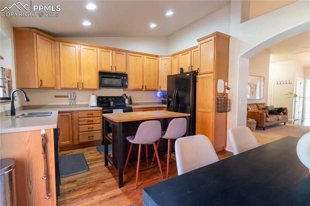 Image 17 of 26: Kitchen featuring arched walkways, a breakfast bar, black appliances, wood