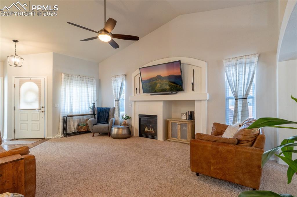 Image 19 of 26: Living area with a fireplace, lofted ceiling, carpet floors, healthy amount