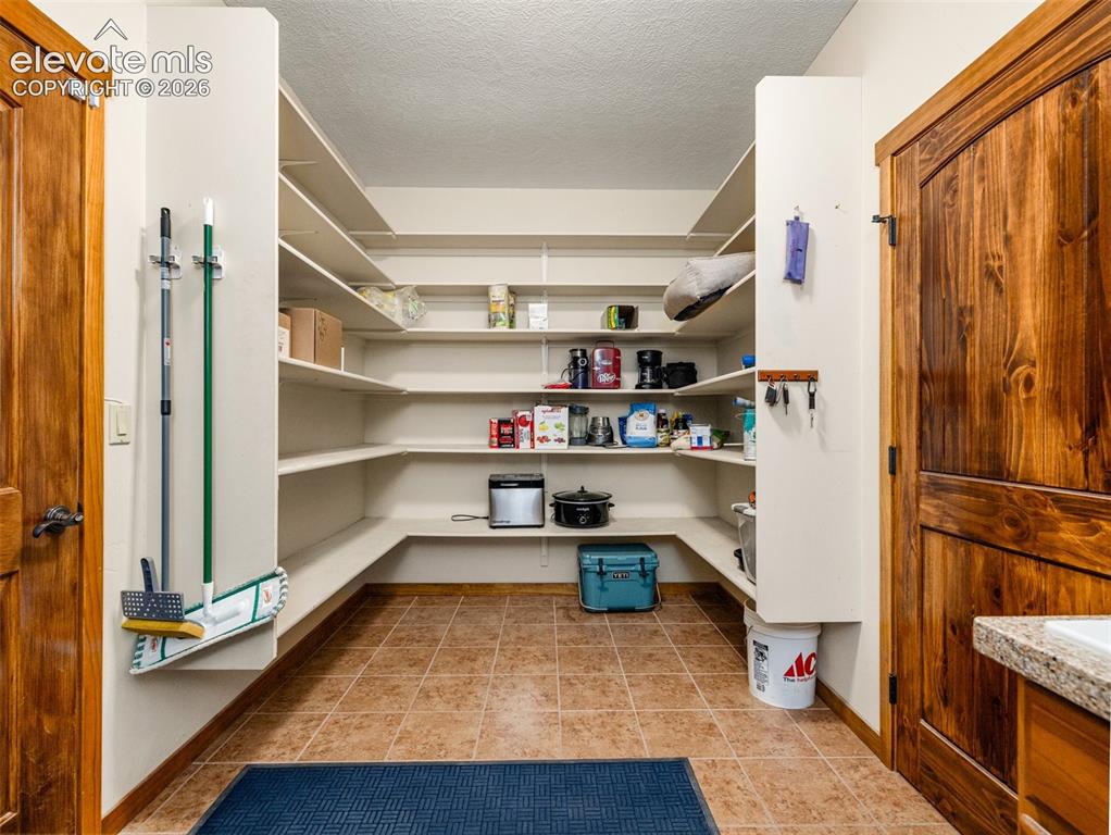 Image 13 of 44: Spacious pantry with extensive built-in shelving, tile flooring, and a natu
