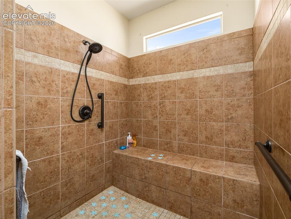 Image 17 of 44: Walk-in shower with full wall tiling, built-in bench, and bronzed fixtures